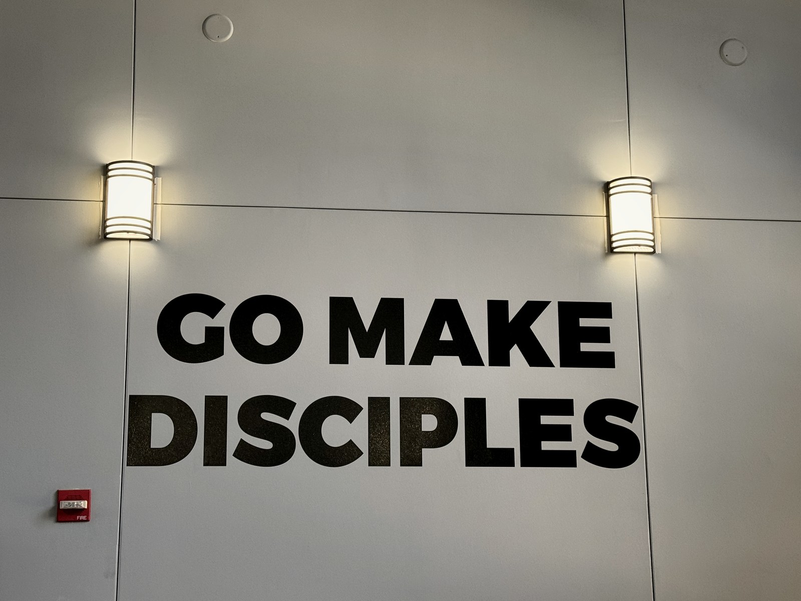 LED wall sconces lighting the GO MAKE DISCIPLES feature wall at BRAVE Church